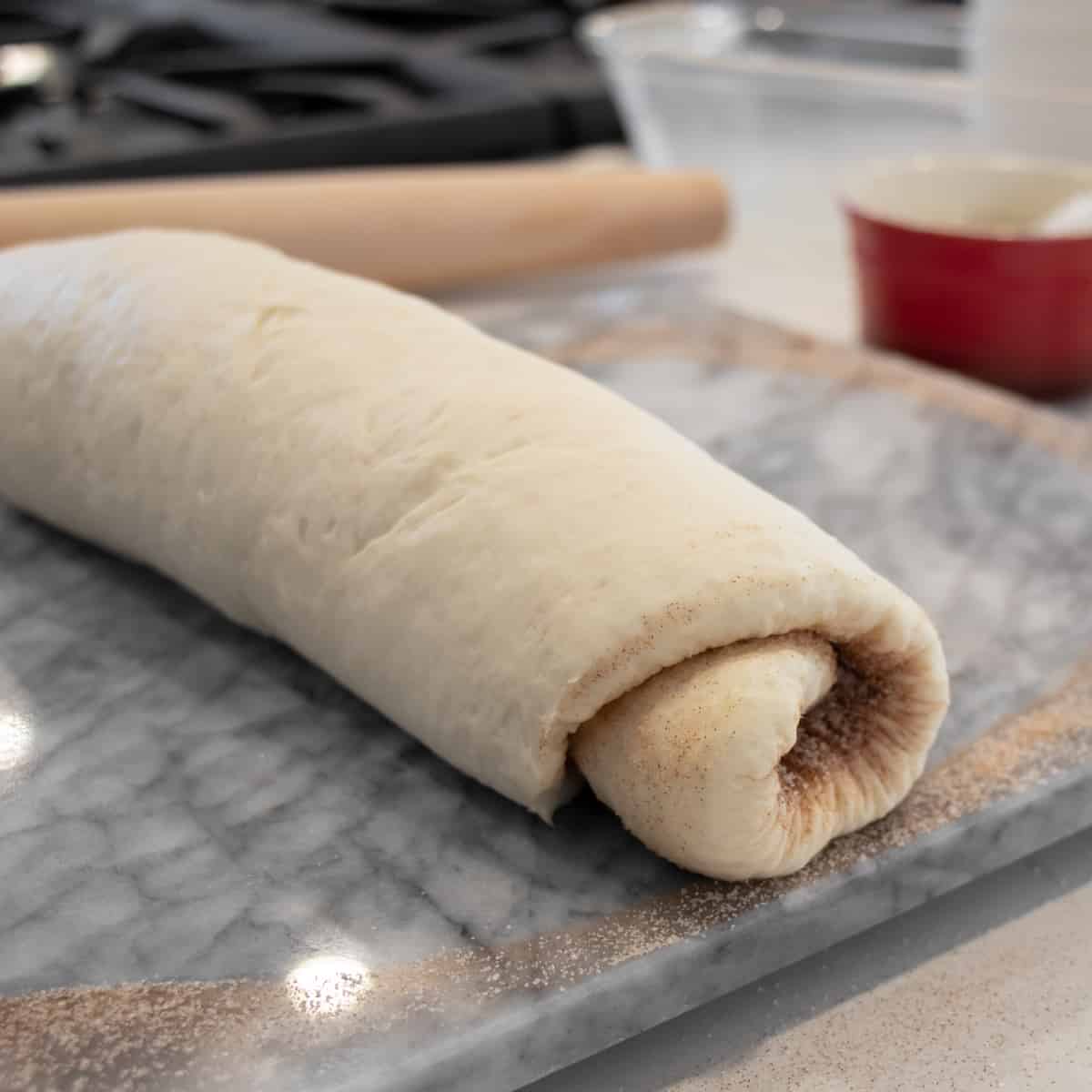 Dough rolled into a log and resting on a marble board.