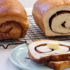 Sliced bread on a plate in front of two loaves on a wire rack.