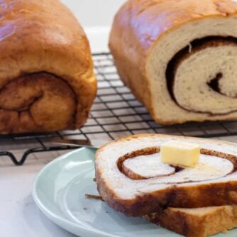 Sliced bread on a plate in front of two loaves on a wire rack.