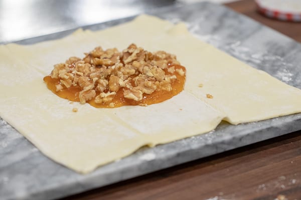 Delicious appetizer recipe of baked brie cheese wrapped in puff pastry with apricot jam and walnuts.
