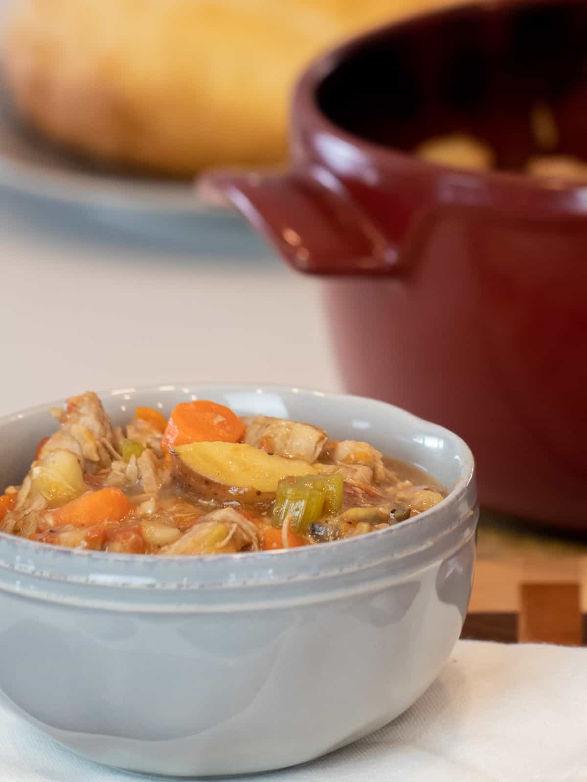 A bowl of stew in front of a red dutch oven.