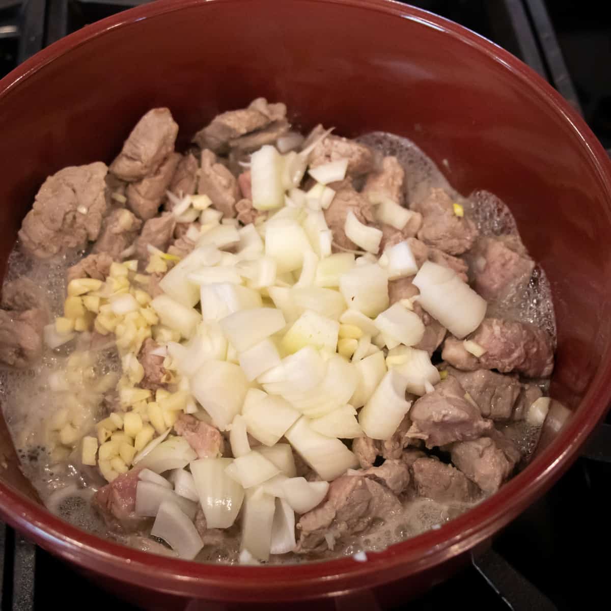 A red pot with pork, garlic and onion cooking.