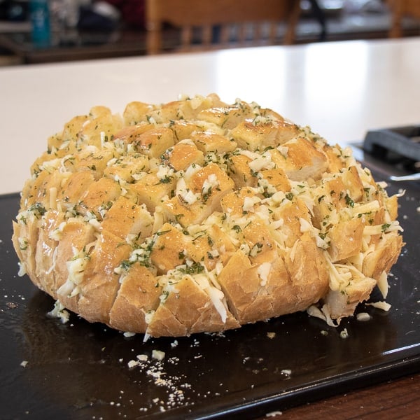 Cheesy pull apart bread made with an artisan rustic round bread loaf, sliced and filled with grated mozzarella cheese, minced garlic, melted butter and parsley. Baked until cheese is bubbly!