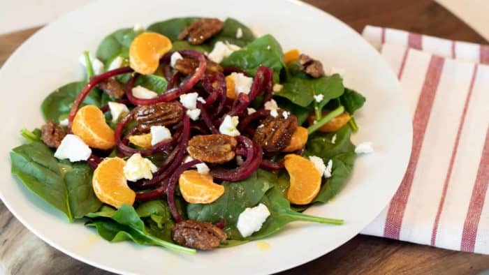 Fresh and healthy salad recipe made with baby spinach, spiralled beets, mandarin oranges, candied pecans and crumbled goat cheese with a honey dijon vinaigrette.
