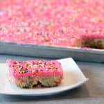Easy recipe for white Texas sheet cake with birthday sprinkles made in a 18x13 half sheet pan. Thin layer cake with pink buttercream frosting for icing. Moist cake made with butter, sour cream, and sprinkles.