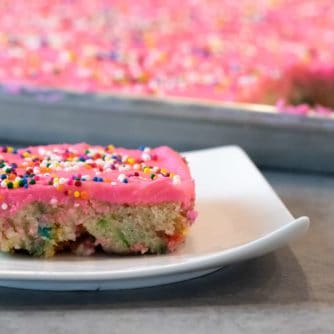 Easy recipe for white Texas sheet cake with birthday sprinkles made in a 18x13 half sheet pan. Thin layer cake with pink buttercream frosting for icing. Moist cake made with butter, sour cream, and sprinkles.