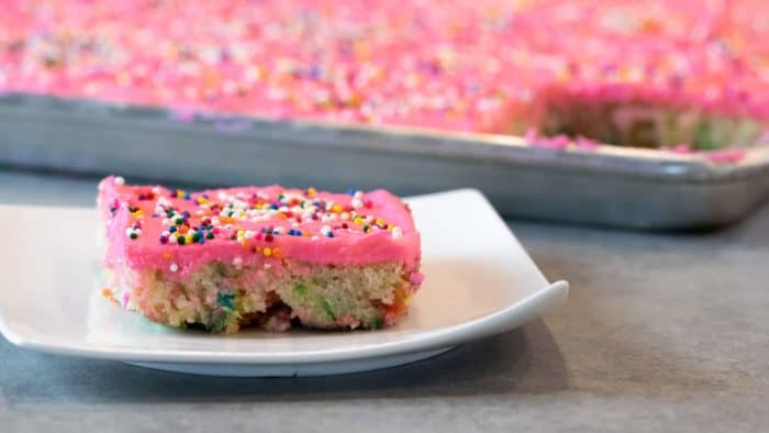 Easy recipe for white Texas sheet cake with birthday sprinkles made in a 18x13 half sheet pan. Thin layer cake with pink buttercream frosting for icing. Moist cake made with butter, sour cream, and sprinkles.