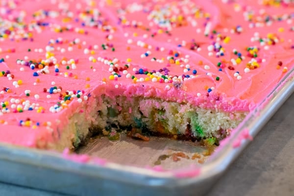 Easy recipe for white Texas sheet cake with birthday sprinkles made in a 18x13 half sheet pan. Thin layer cake with pink buttercream frosting for icing. Moist cake made with butter, sour cream, and sprinkles.