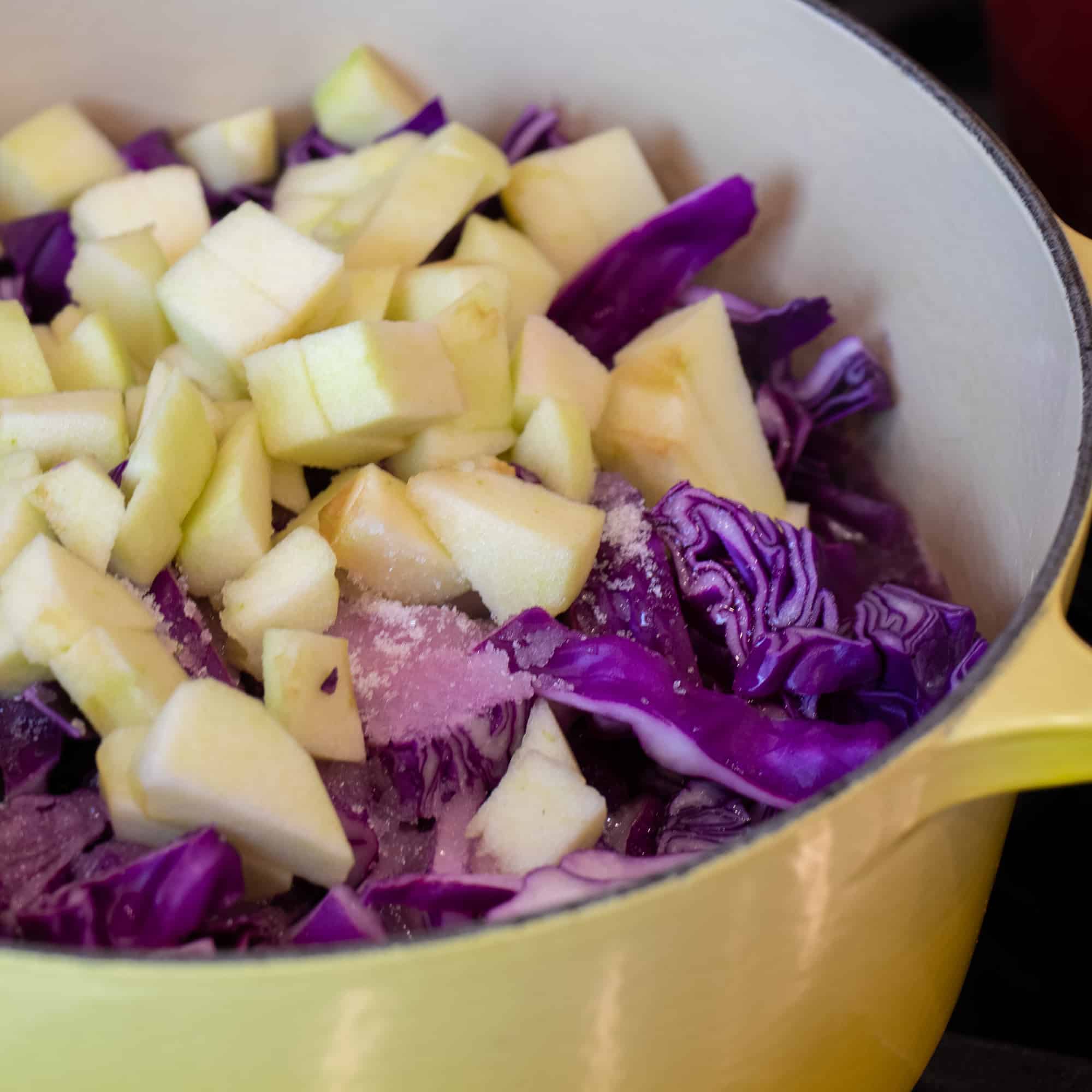 A dutch oven full of chopped red cabbage and diced apples with sugar and vinegar