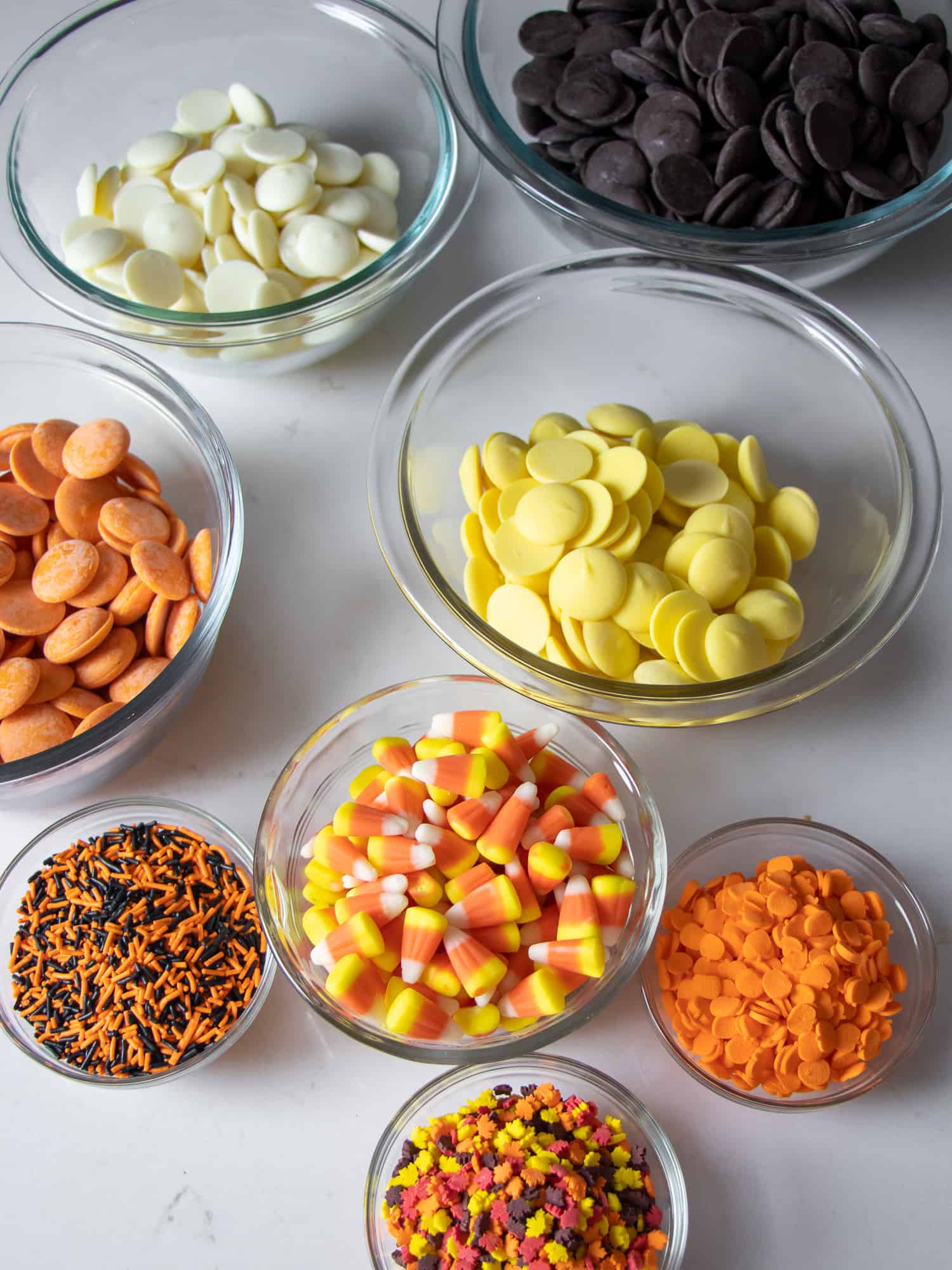 Overhead picture of bowls filled with ingredients of chocolate, sprinkles and candy corn.