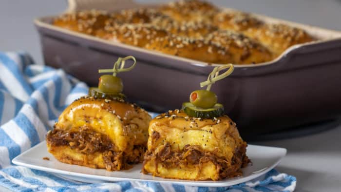 Two sliders on a plate in front of a baking dish.