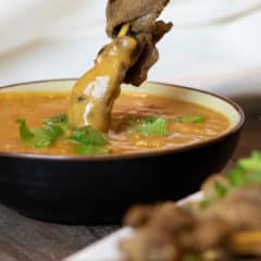 Dipping a beef satay skewer in a bowl of Thai peanut sauce