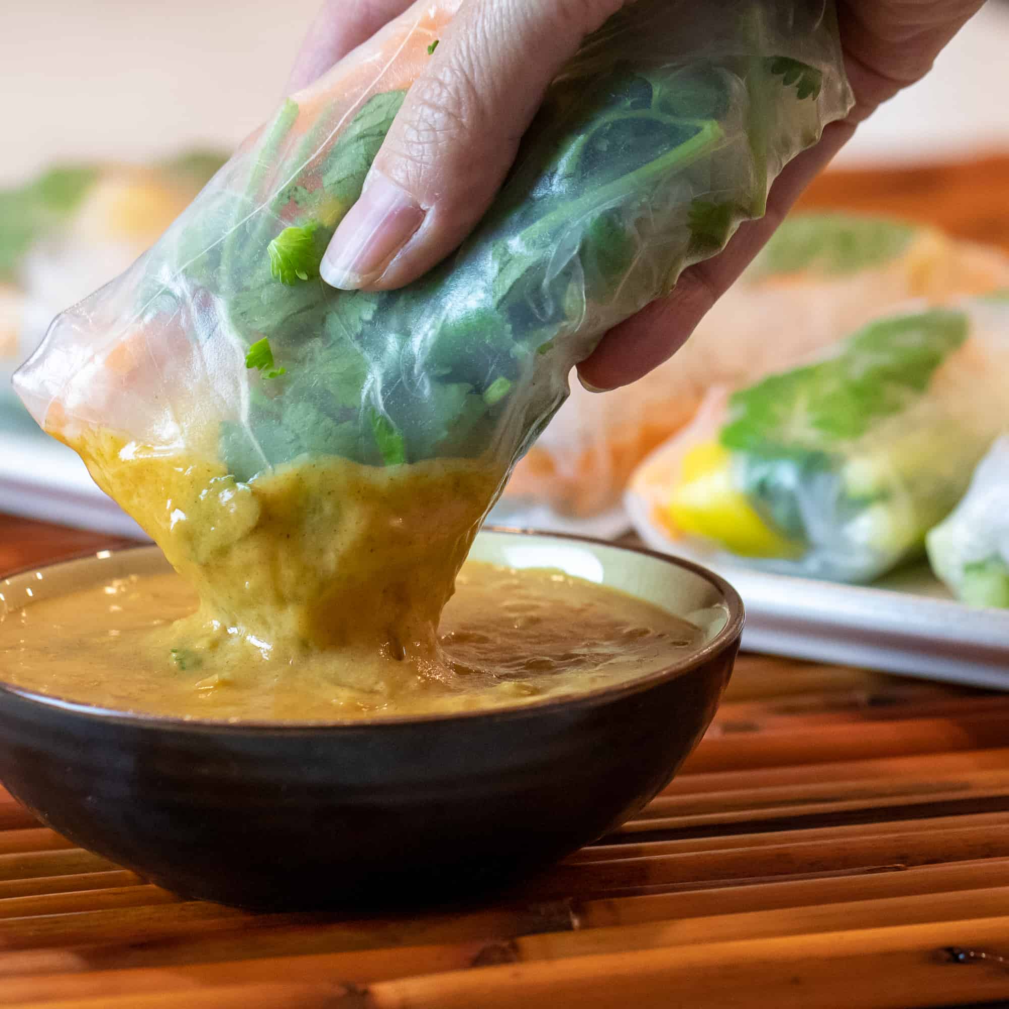 Cold salad spring roll being dipped in a bowl of peanut sauce