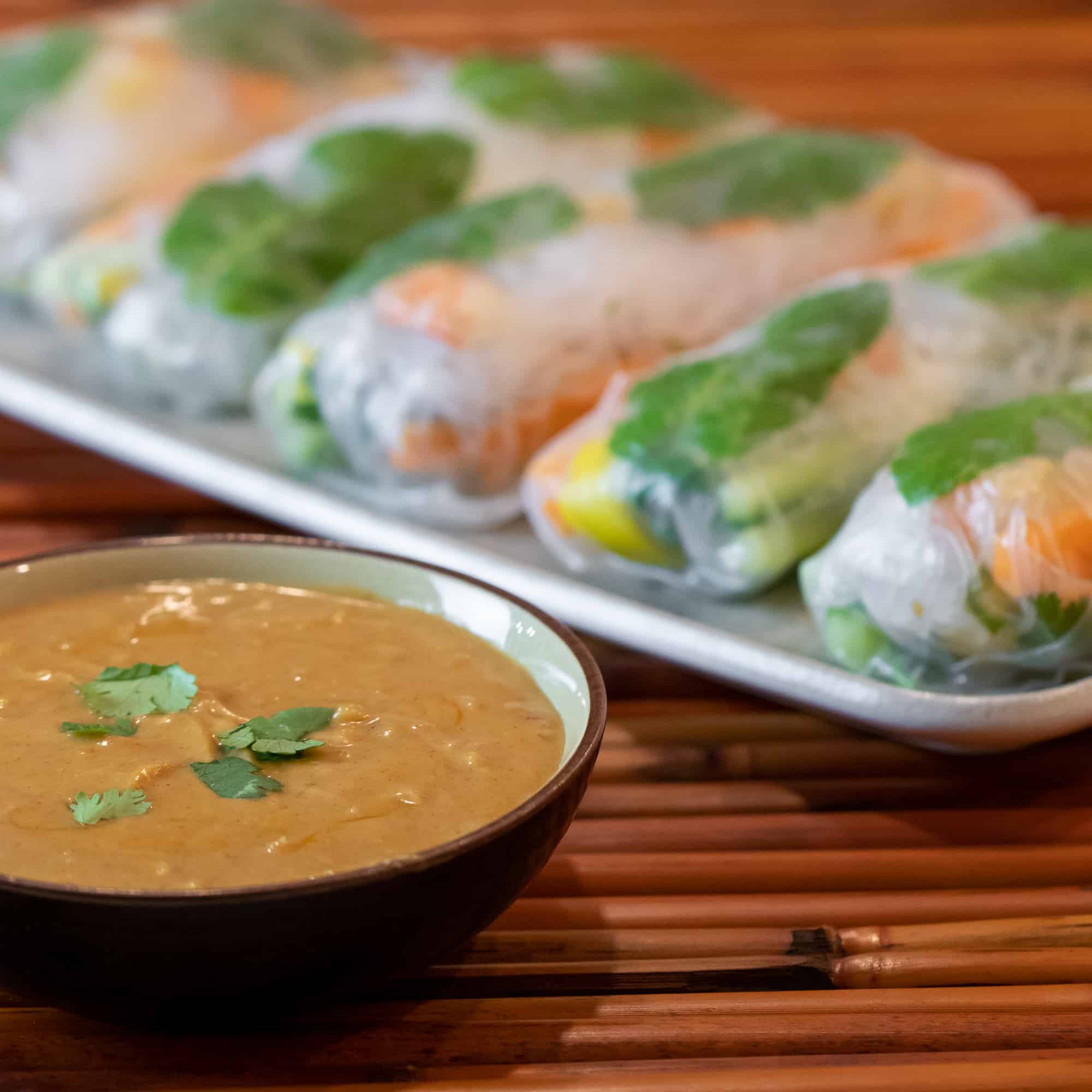 A bowl of peanut sauce with a plate of Thai cold spring rolls