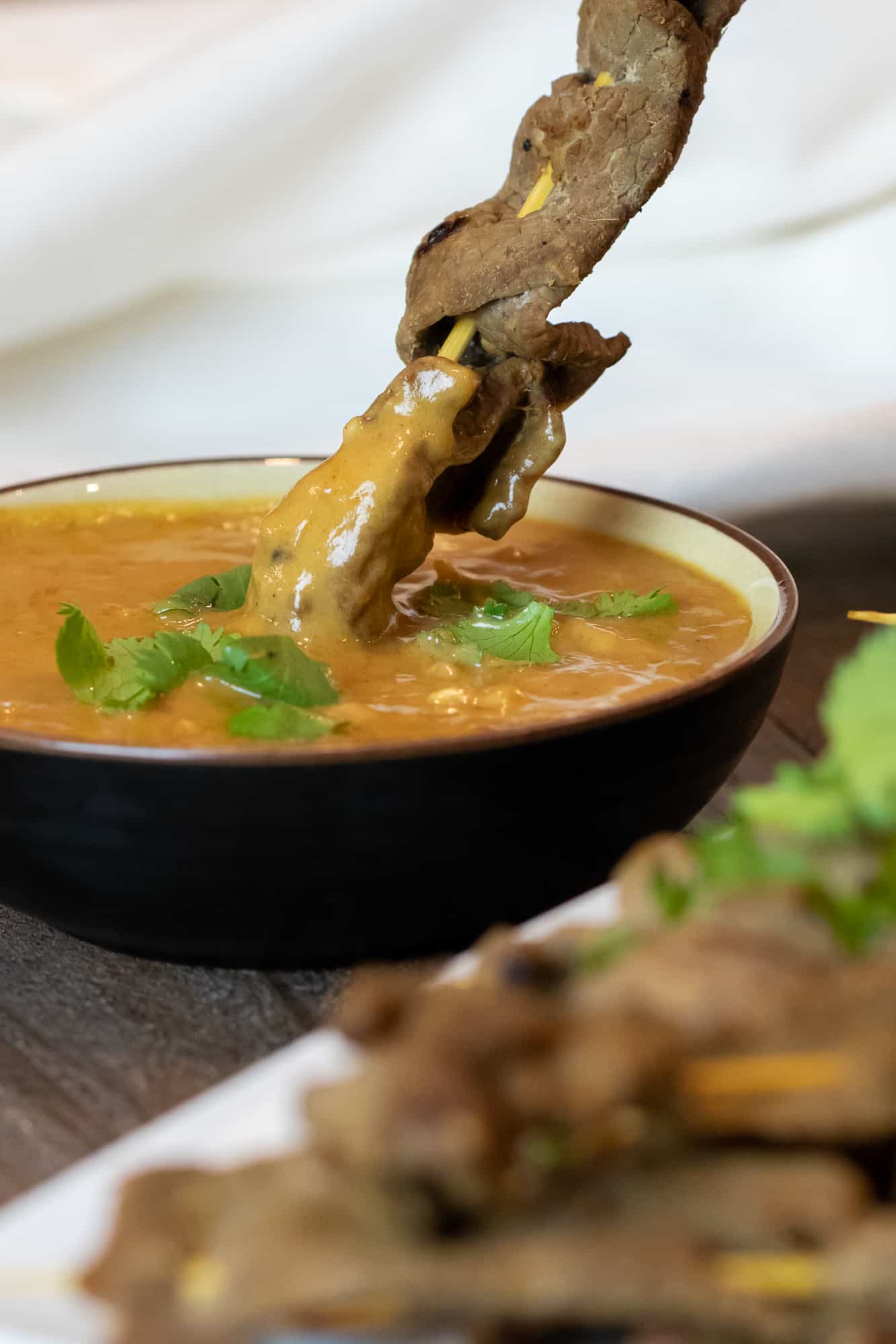 Beef satay dipped in a bowl of Thai peanut sauce