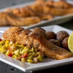 An oven baked salmon fillet on a plate with mini potatoes and succotash.