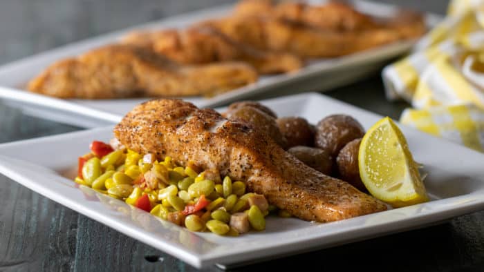 An oven baked salmon fillet on a plate with mini potatoes and succotash.