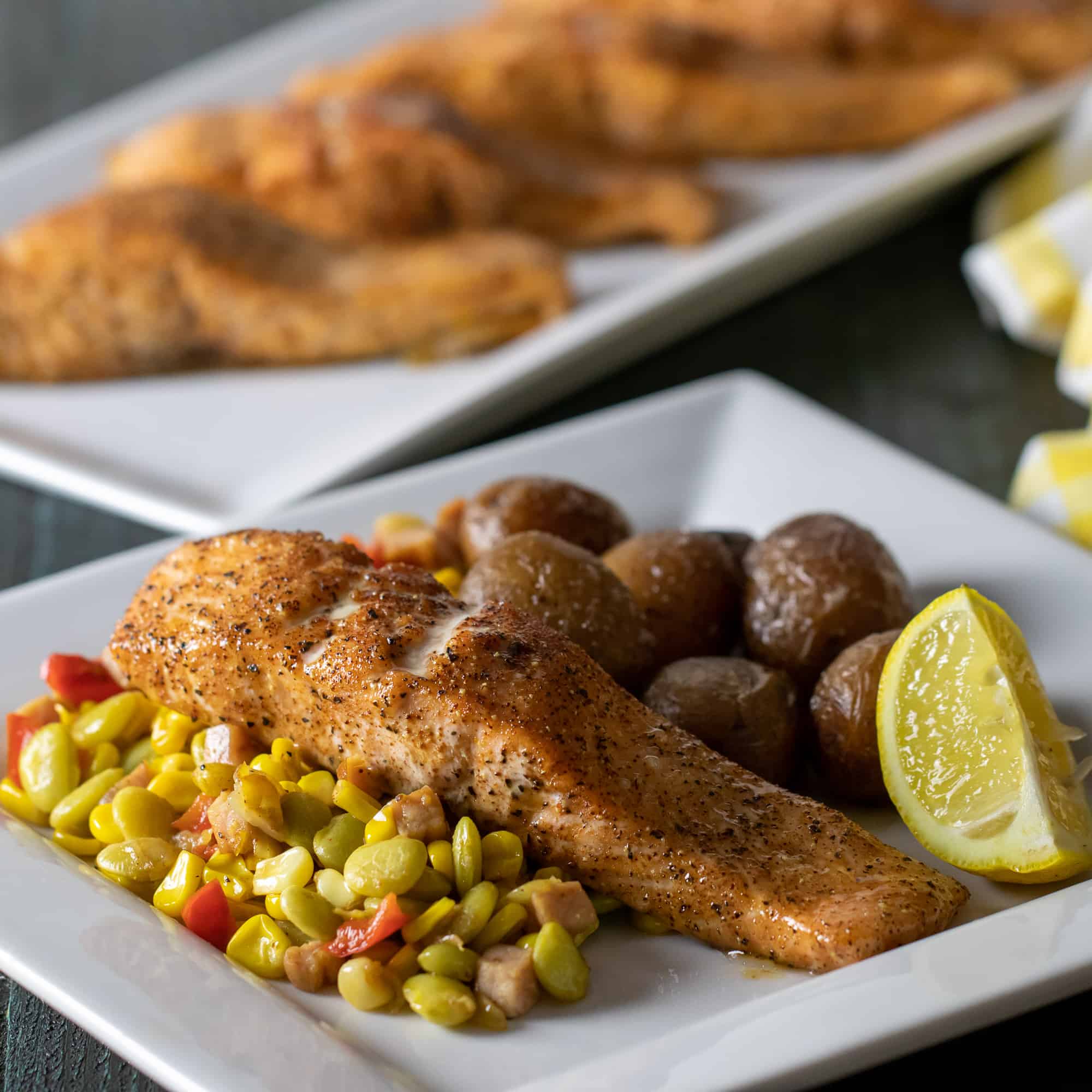 Angled picture of plate of baked salmon fillets with potatoes, corn and lima beans.