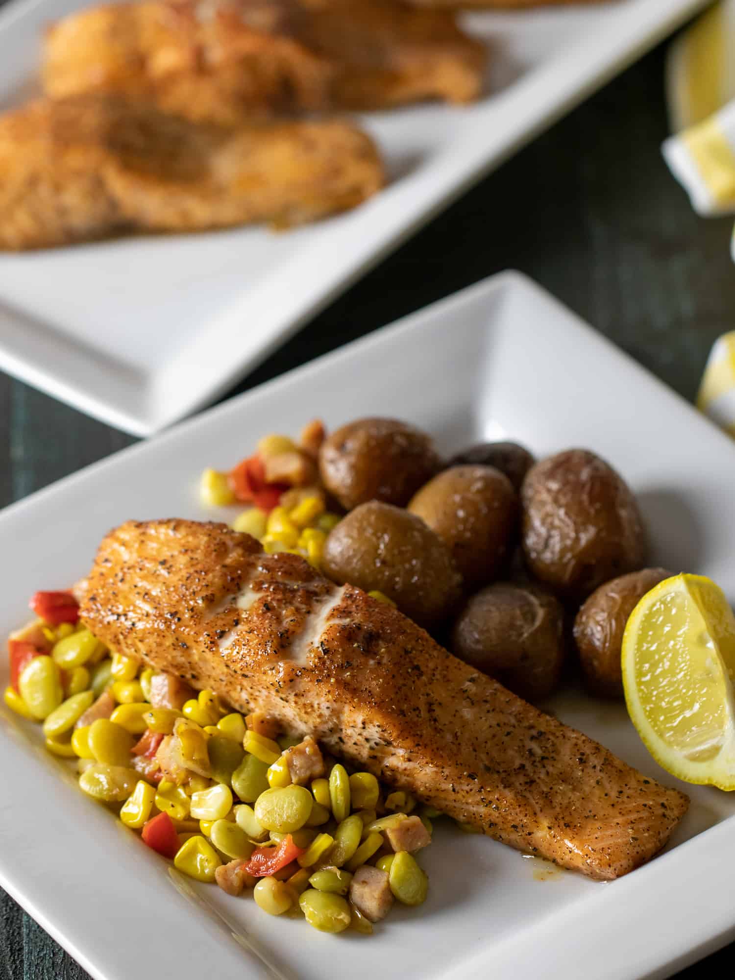 Overhead picture of plate of baked salmon fillets with potatoes, corn and lima beans.