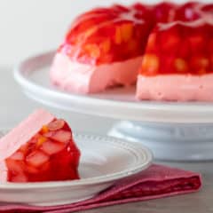 A Jello mold ring with fruit salad on a cake stand with a slice on a plate.