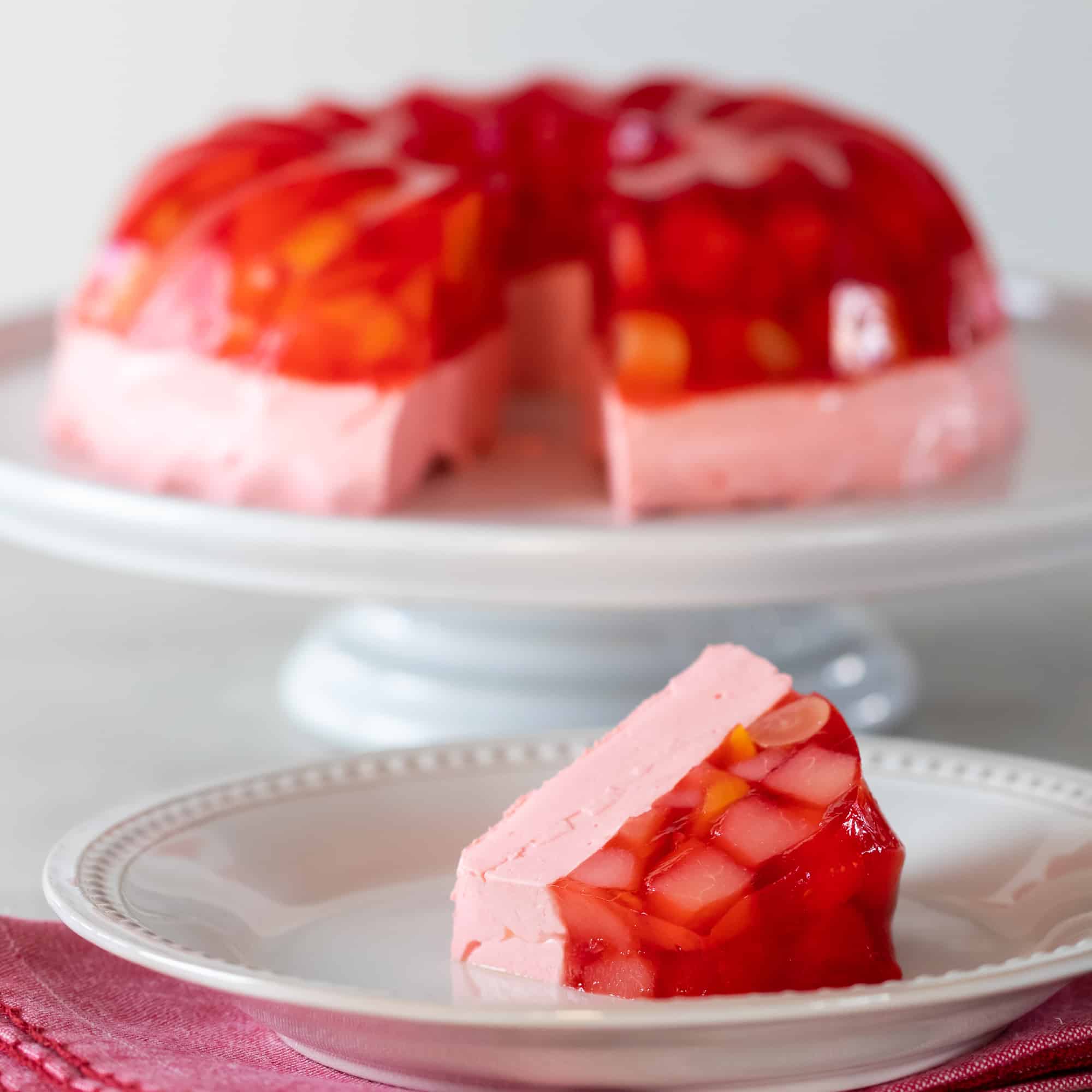 A Jello mold ring with fruit salad on a cake stand with a slice on a plate.