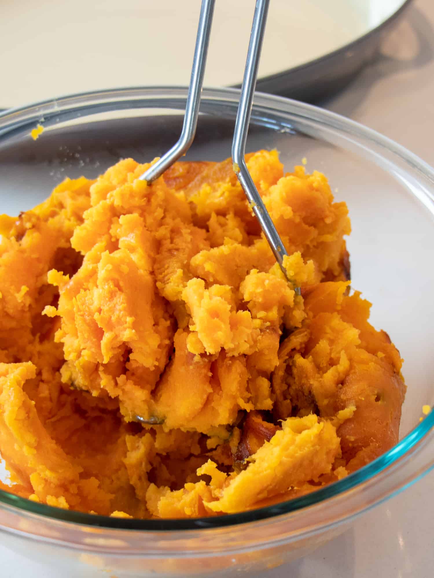 A bowl of cooked sweet potatoes being mashed with a potato hand masher.