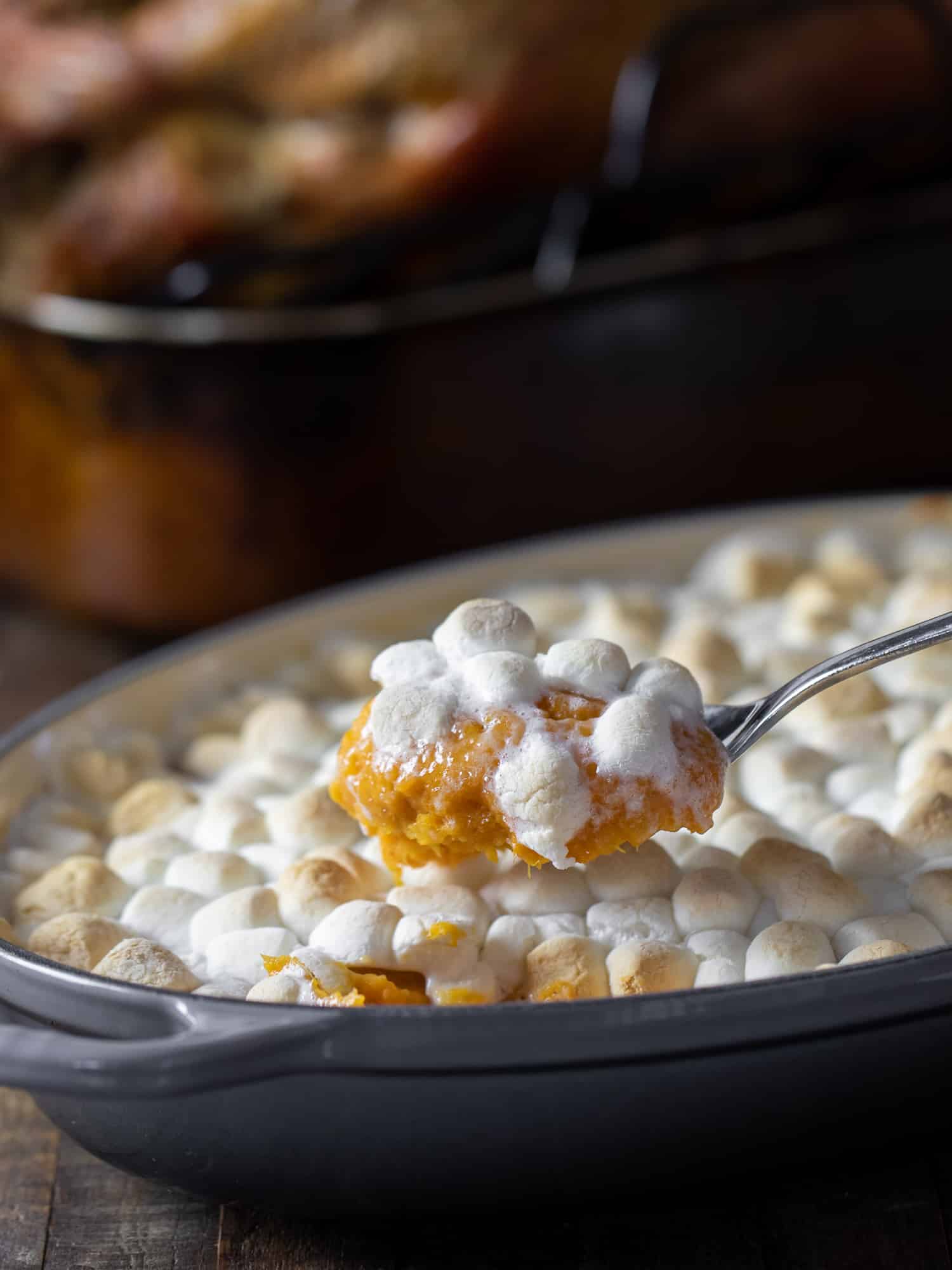 Scooping a spoonful of sweet potato casserole with toasted marshmallow topping