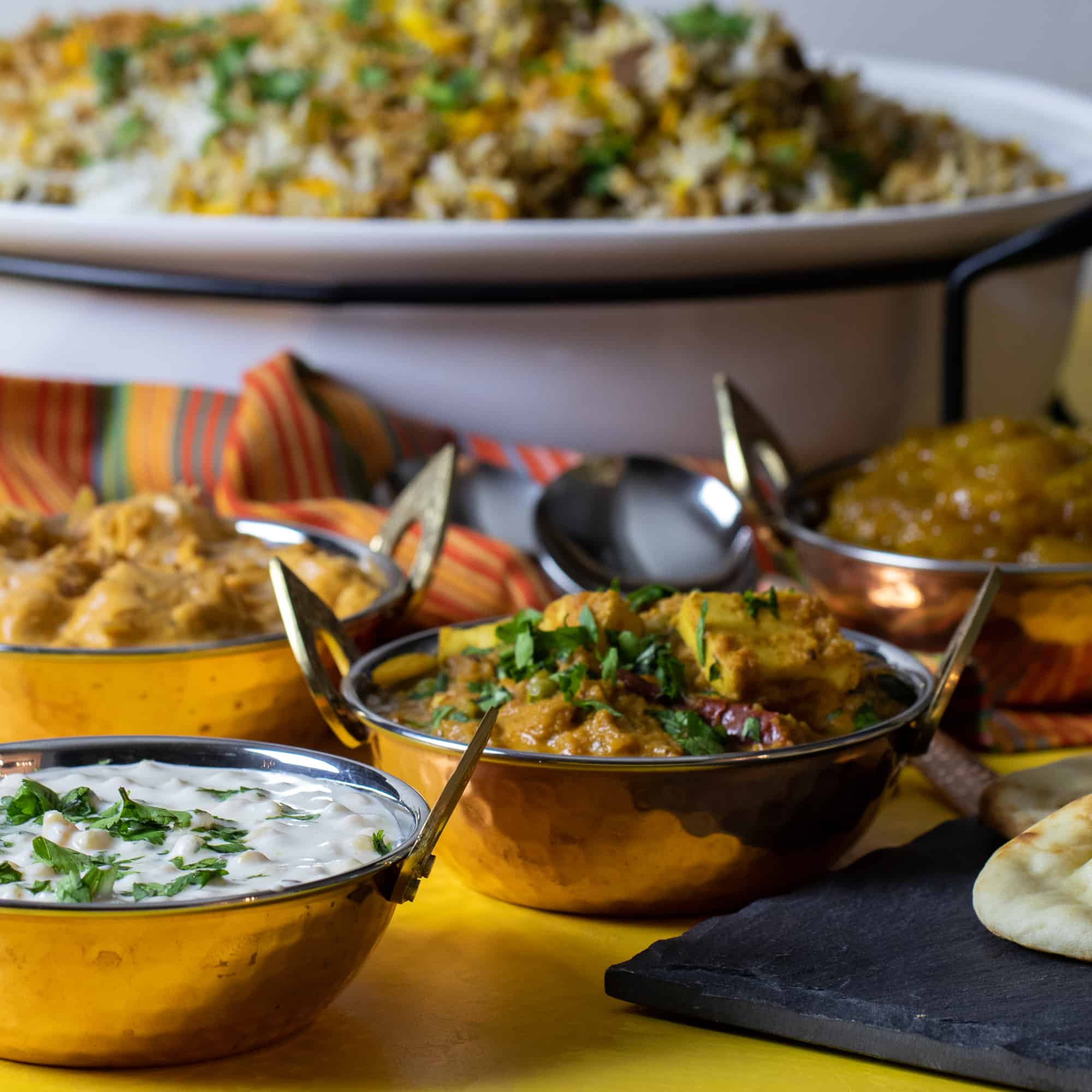 A photo of a full indian dinner including biryani, butter chicken, raita, mango chutney and matar paneer.