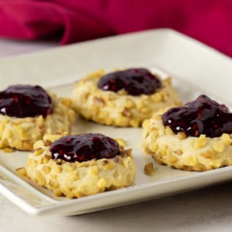 Classic recipe for thumbprint cookies rolled in chopped walnuts with a dollop of raspberry jam on top. Easy recipe and perfect for Christmas holiday baking.