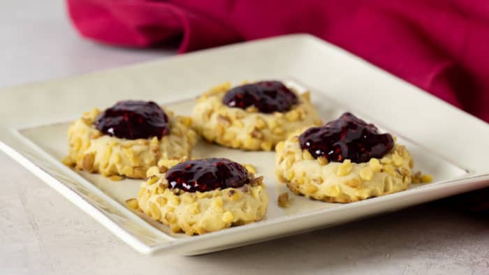 Classic recipe for thumbprint cookies rolled in chopped walnuts with a dollop of raspberry jam on top. Easy recipe and perfect for Christmas holiday baking.