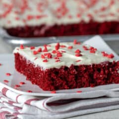 A slice of red velvet sheet cake on a plate with heart sprinkles.