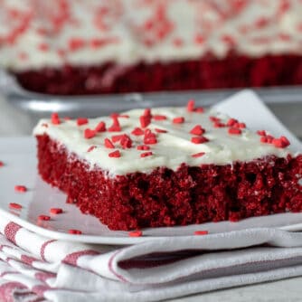 A slice of red velvet sheet cake on a plate with heart sprinkles.