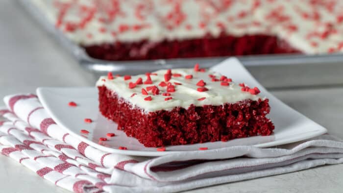 A slice of red velvet sheet cake on a plate with heart sprinkles.