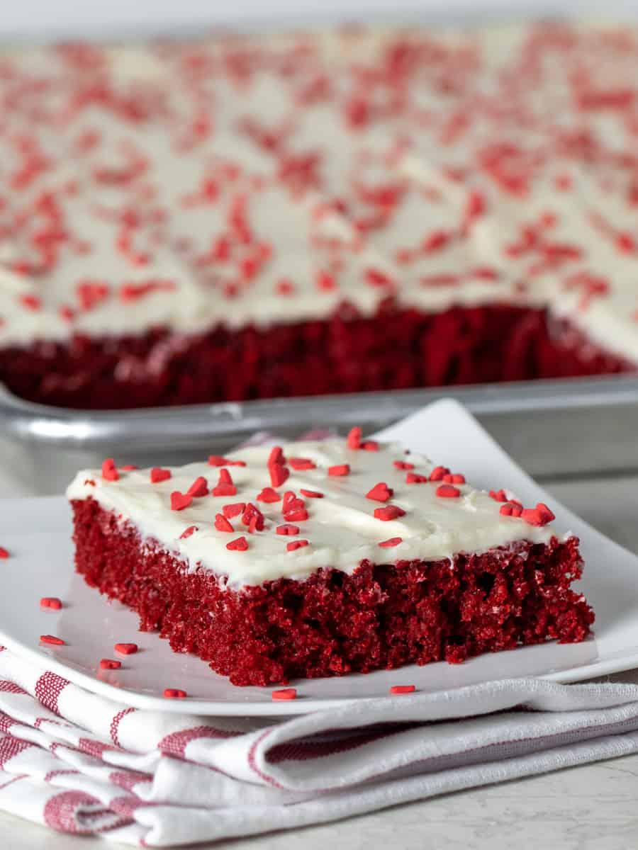 A tall image of a plate of dessert with a sheet cake in the background.