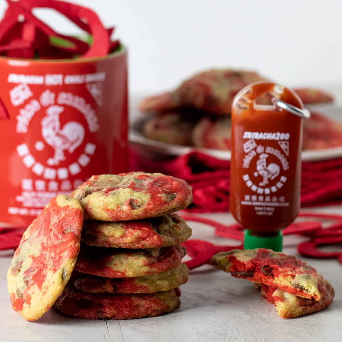 A stack of cookies next to a mug and bottle of Sriracha sauce