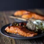 A close up picture of a dinner plate with salmon and baked potato.