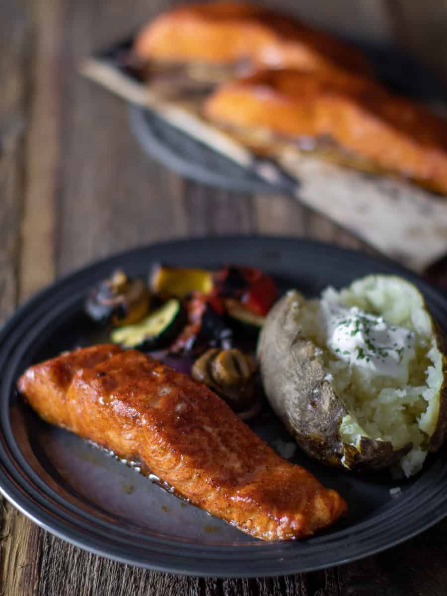 A plate of food with a plank with two fillets of salmon in the background.