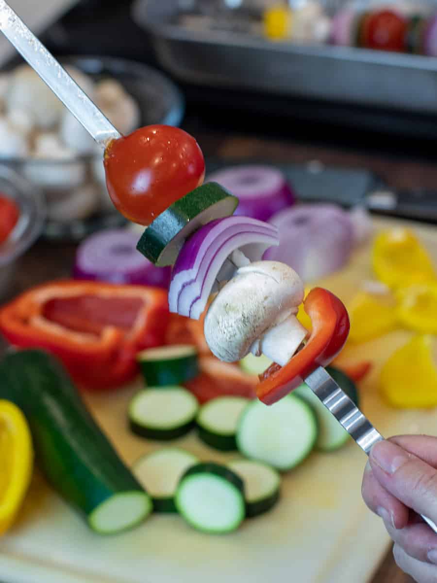 Threading chopped vegetables on a metal skewer.