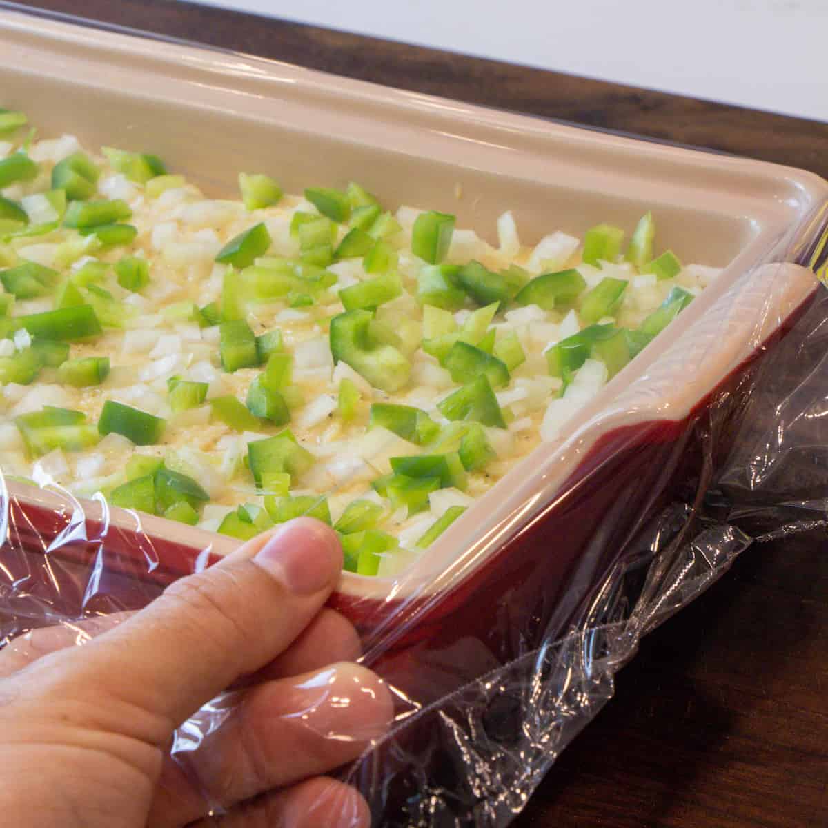 Covering the dish with plastic wrap.