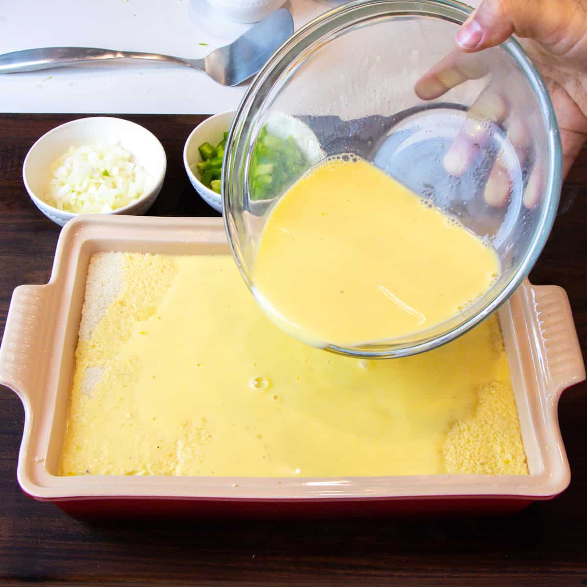 A bowl of beaten eggs and milk being poured over bread.