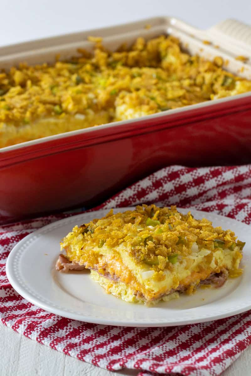 A slice of casserole on a plate in front of baking dish.