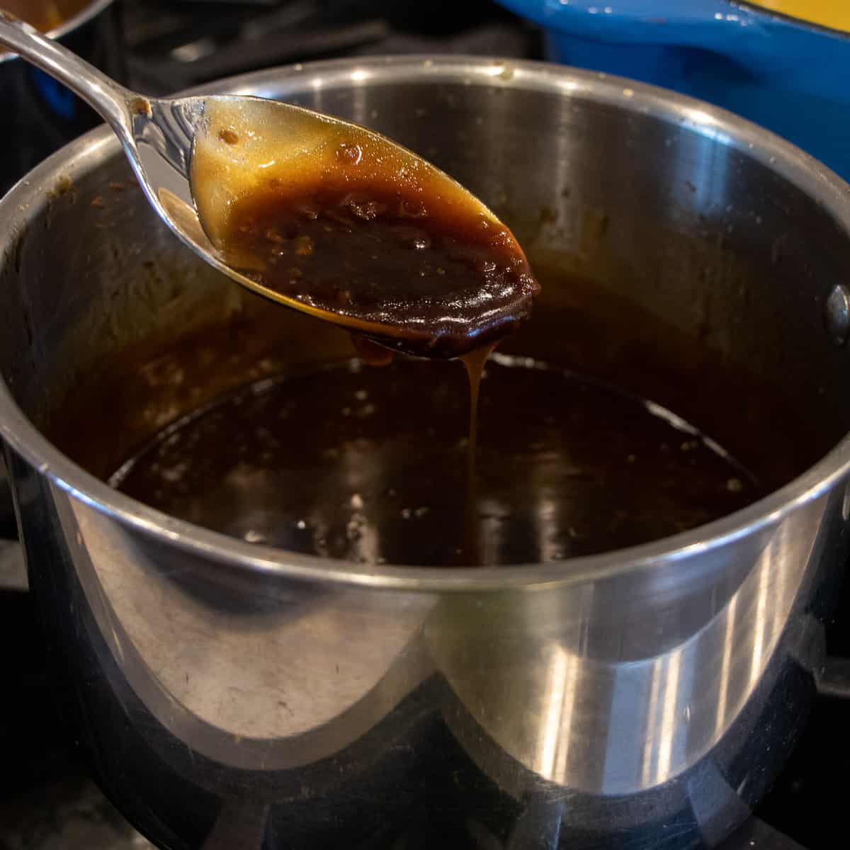 A spoon of sauce lifted out of a saucepan.