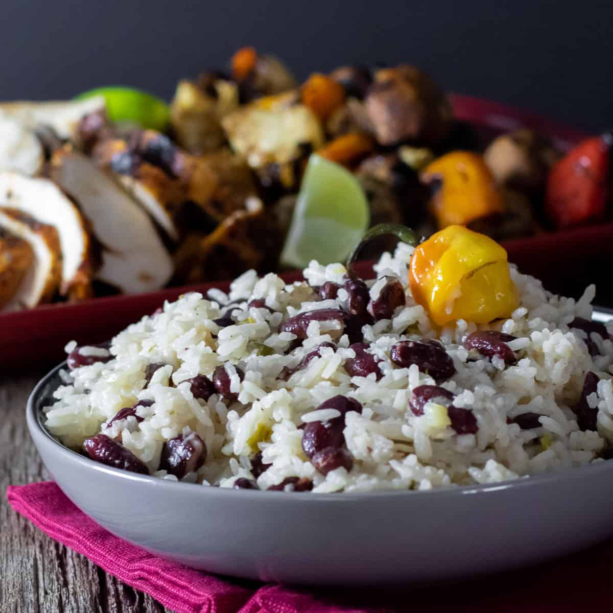 A bowl of rice and beans with a platter of chicken and vegetables in the background.