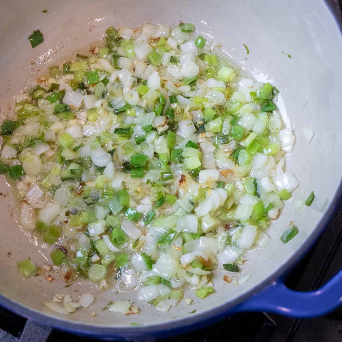 Onions and scallions sautéing in a dutch oven.
