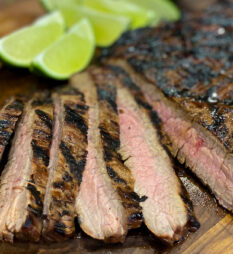 Flank Steak on a cutting board with lime wedges.