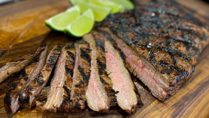 Flank Steak on a cutting board with lime wedges.