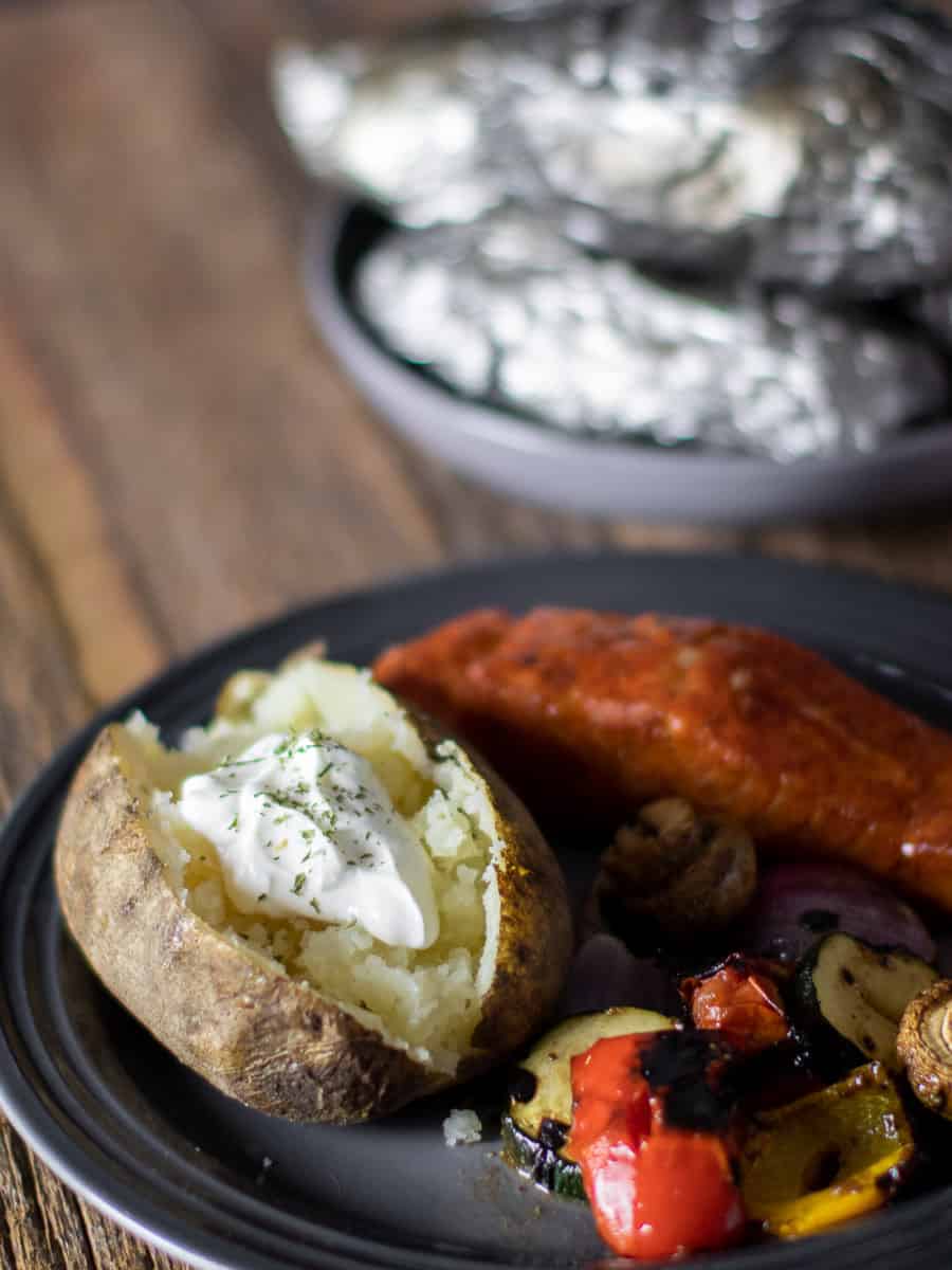 A plate with a baked potato, grilled salmon and vegetables.