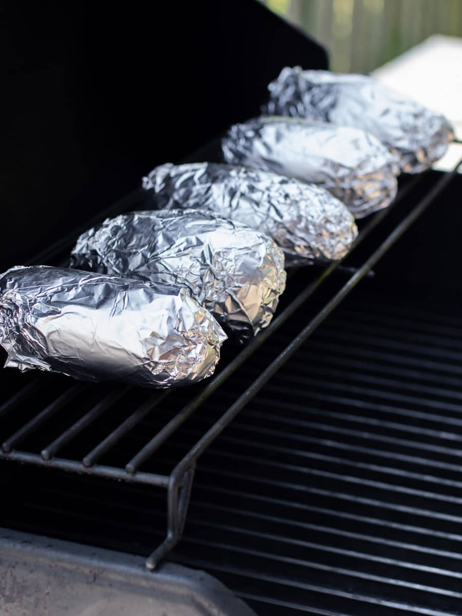 Wrapped potatoes on the upper rack of a grill.