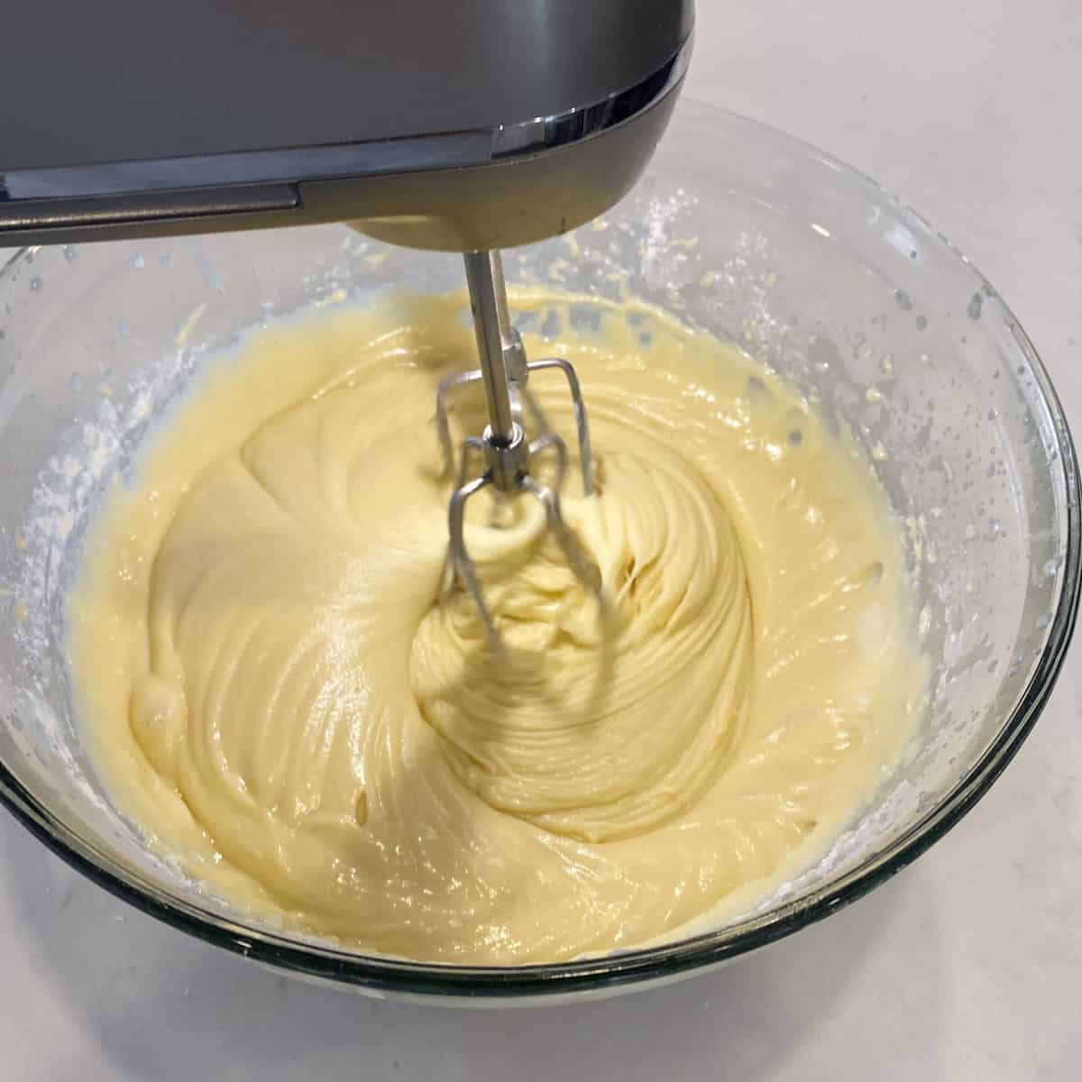 A bowl of cake batter being mixed with an electric mixer.