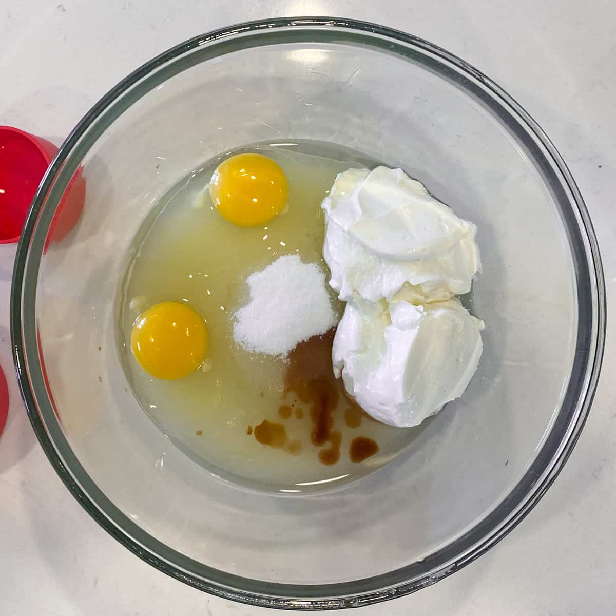 A bowl of white sugar, eggs, sour cream, oil and vanilla.
